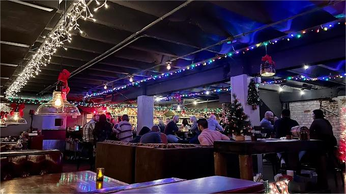 Restaurant interior decorated with Christmas lights, people seated at tables, festive atmosphere.