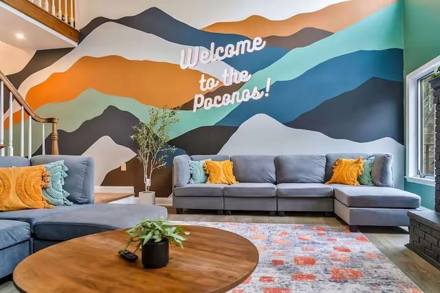 A living room with a couch , coffee table , and a mural on the wall. that says 'Welcome to the Poconos!'