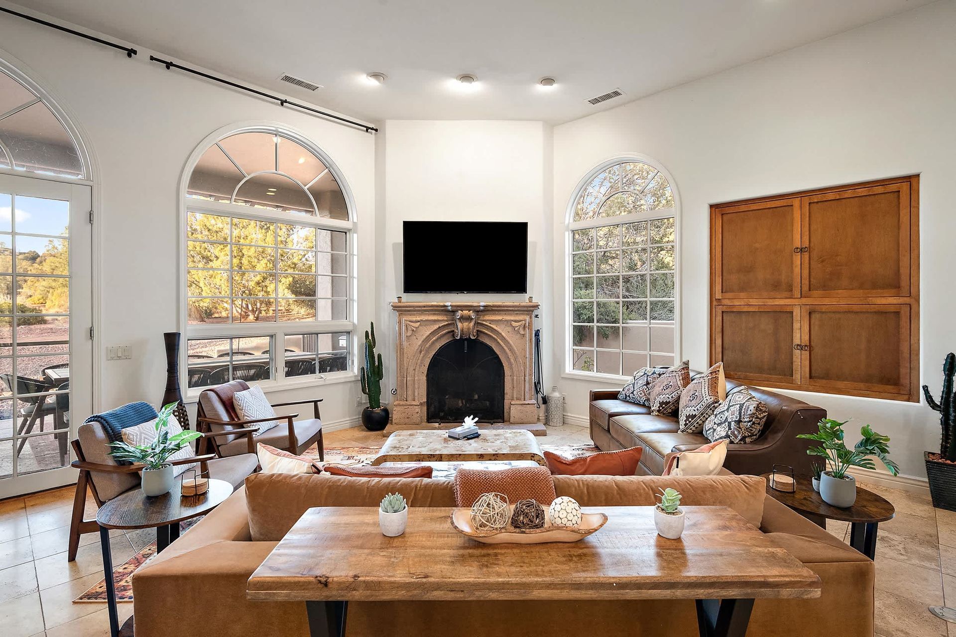 Bright living room with arched windows, fireplace, large TV, and wooden coffee table with decor