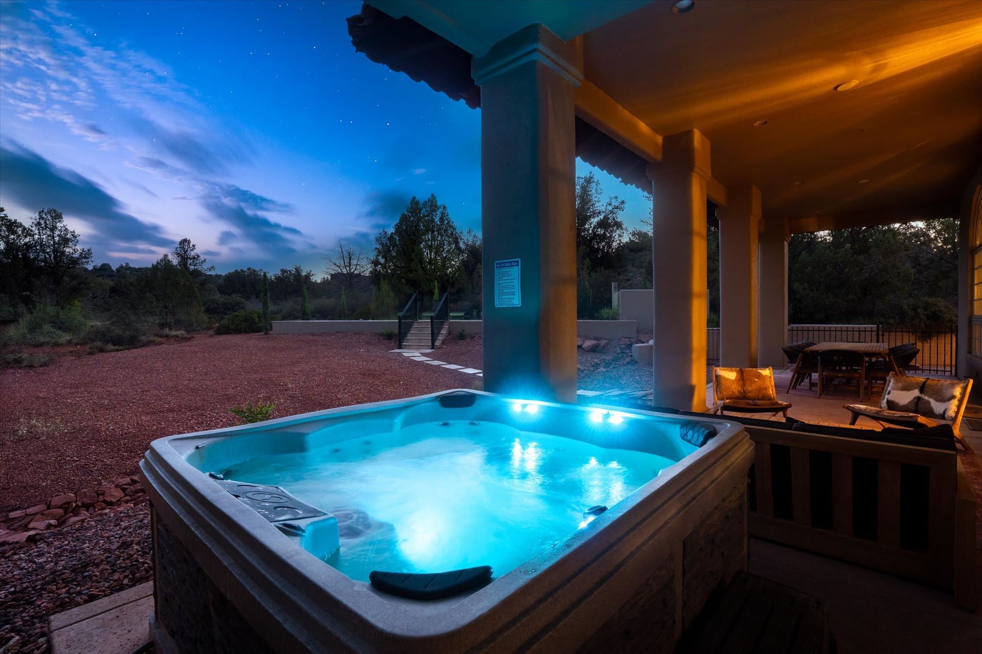 Blue-lit hot tub on a porch at dusk overlooking a wooded landscape