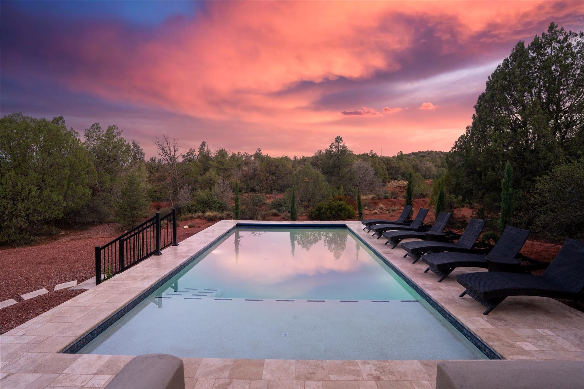 Poolside lounge chairs at sunset with a pink sky and desert landscape