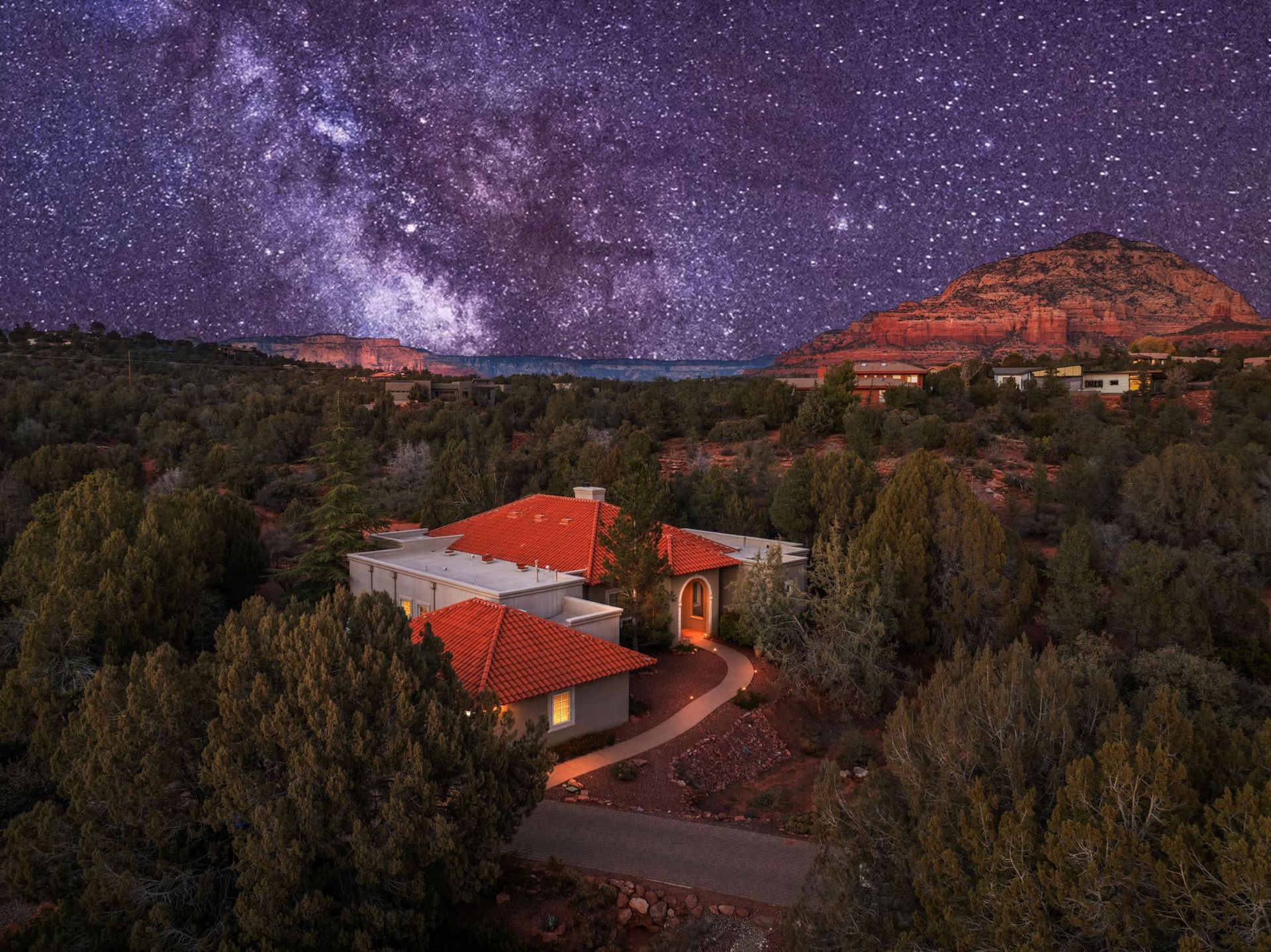 Red-roofed house in a wooded valley under a star-filled night sky