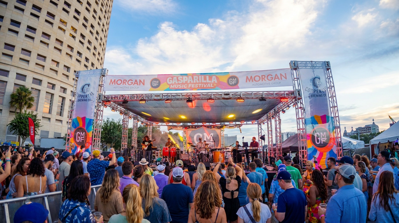 Crowd watching a lively outdoor concert on a city stage at sunset, with colorful lights and banners.