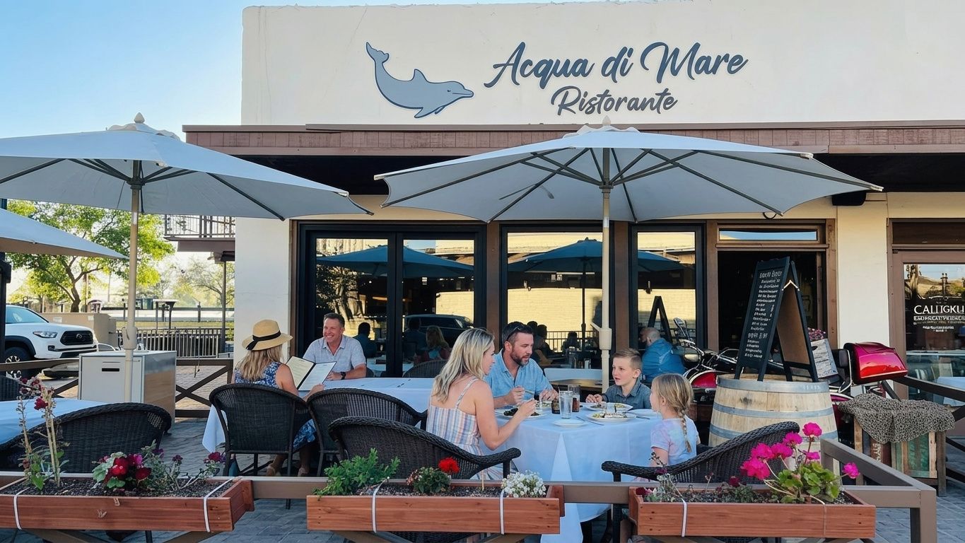 People dining outdoors under umbrellas at Aqua de Mare restaurant with flowers and potted plants in front