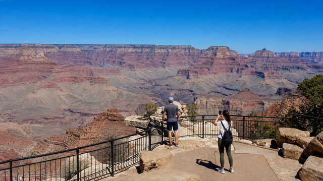 Scenic canyon overlook with a few visitors on a stone path and metal railing under clear sky