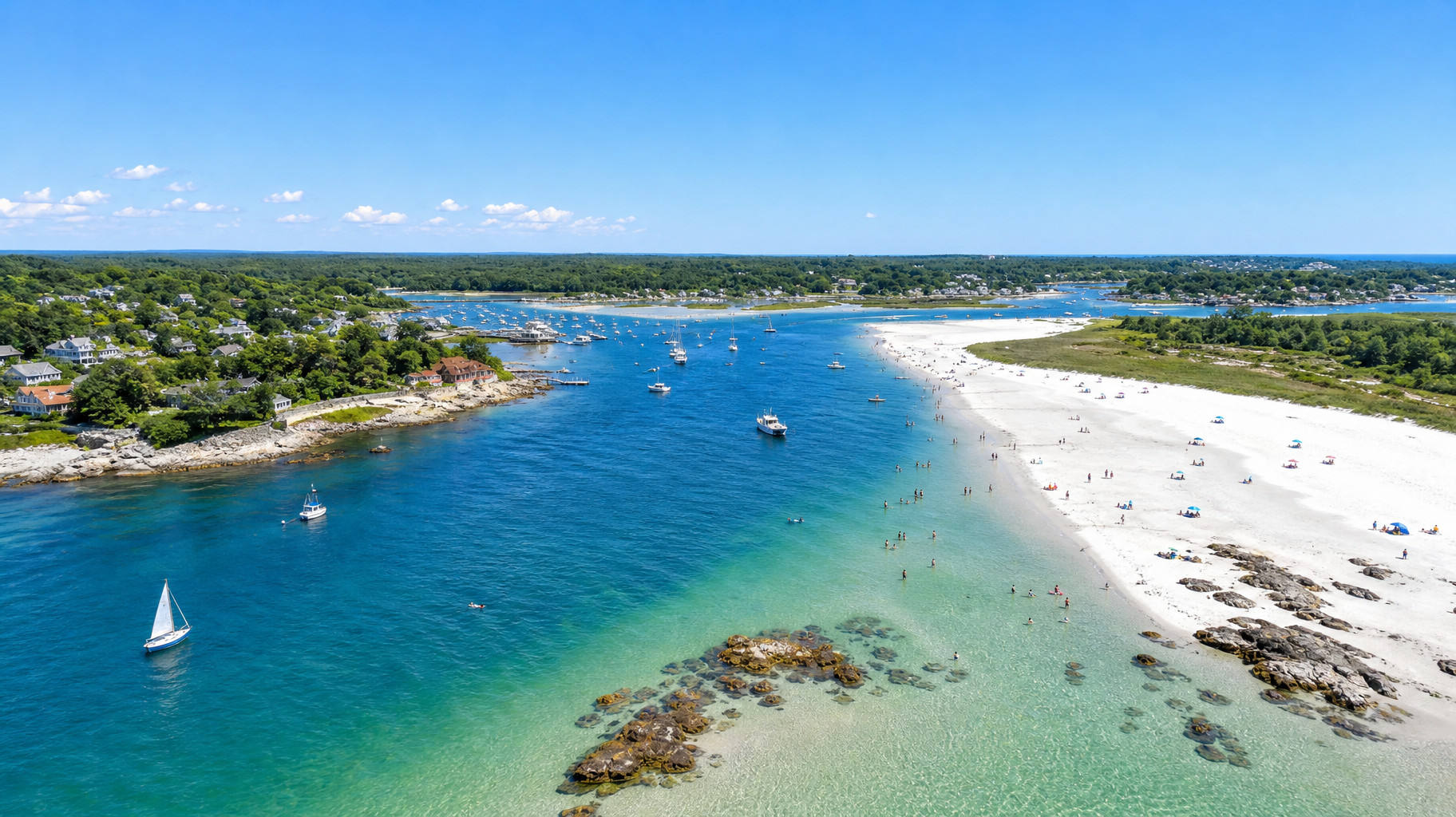 Turquoise bay with sailboats, white sandy shore, and green coastline under a clear blue sky