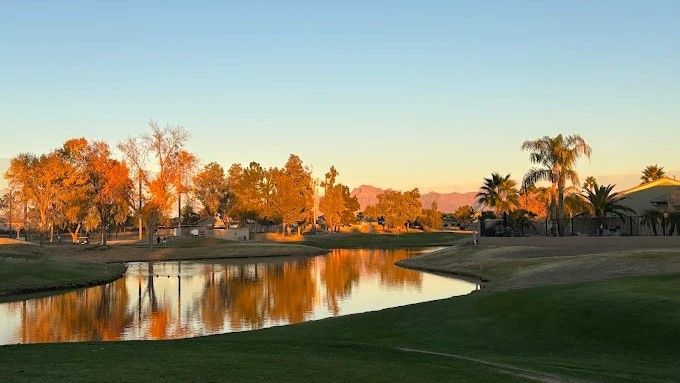 Water reflects trees at sunset on a golf course.