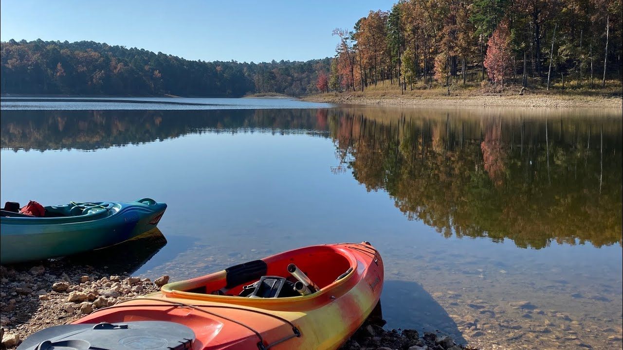 Two kayaks on a lake shore with reflections of trees in the water.