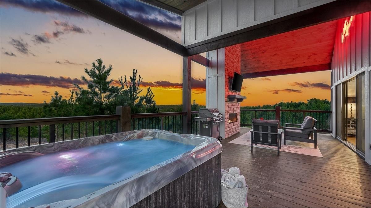 Outdoor deck with hot tub, fireplace, seating, and a sunset view.