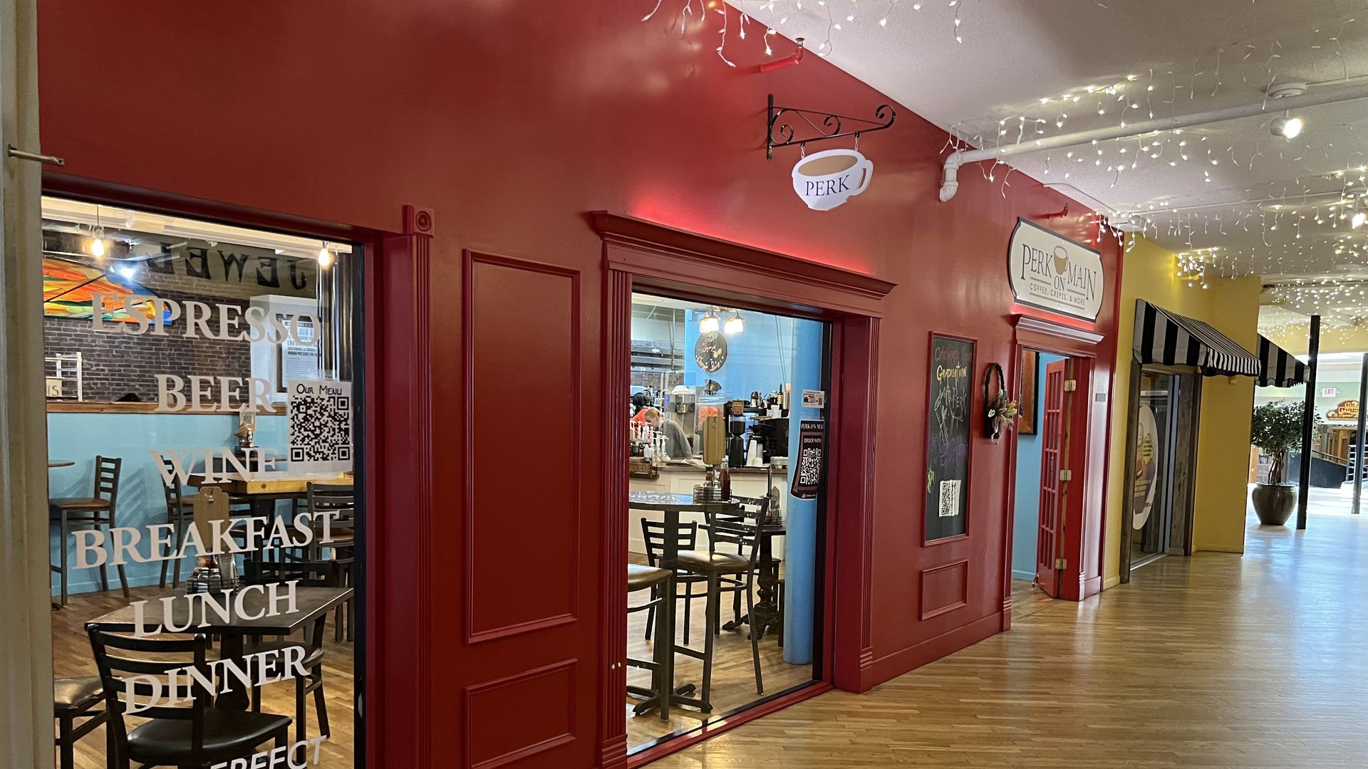 A cafe with a deep red exterior, large windows, and a bowl logo above the entrance, situated in an indoor corridor.