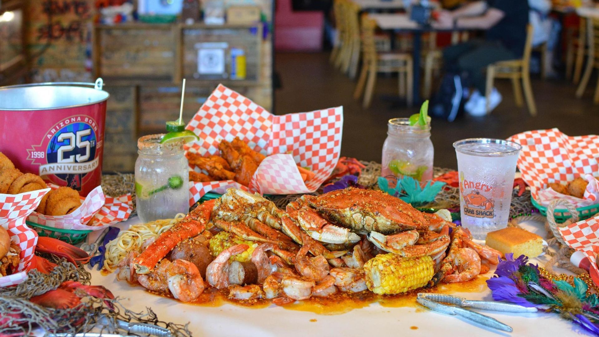 Seafood boil with crab, shrimp, corn, and drinks on a table in a restaurant.