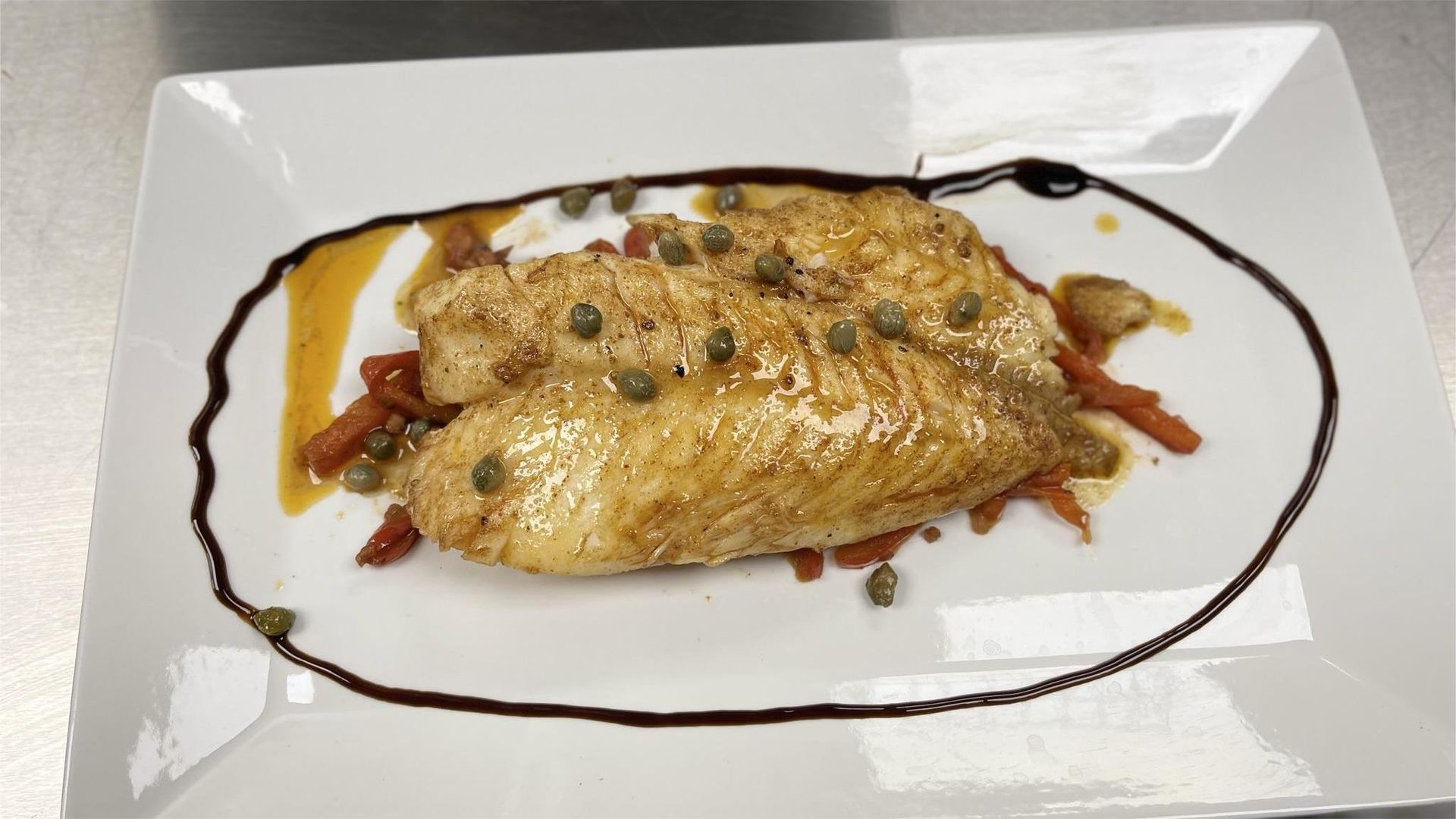 Plate of pan-seared fish with capers, atop roasted tomatoes, drizzled with balsamic glaze.