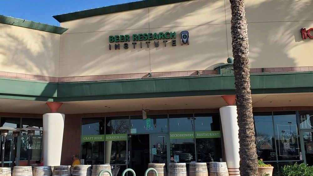Exterior of the Beer Research Institute, a shop in a strip mall with a green awning and barrel accents.
