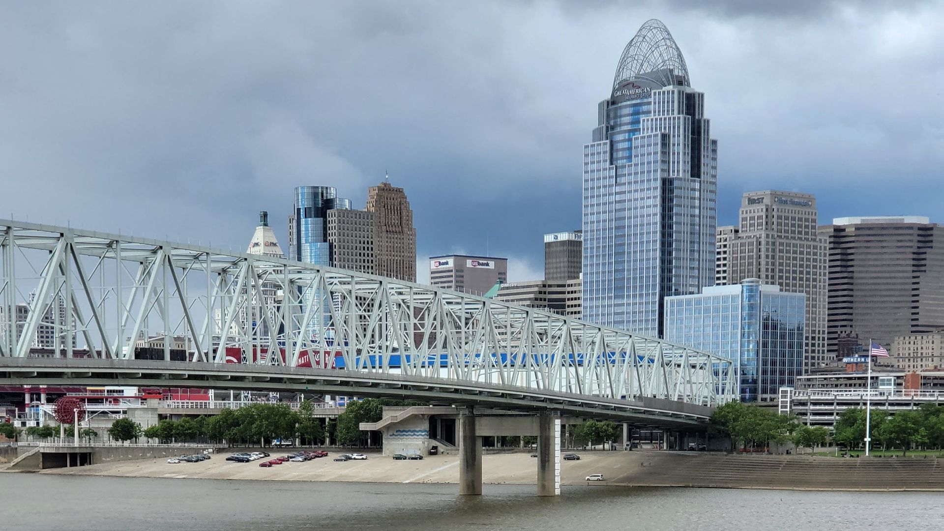 City skyline with bridge over a river, including a tall, pointed-top building. Cloudy sky.