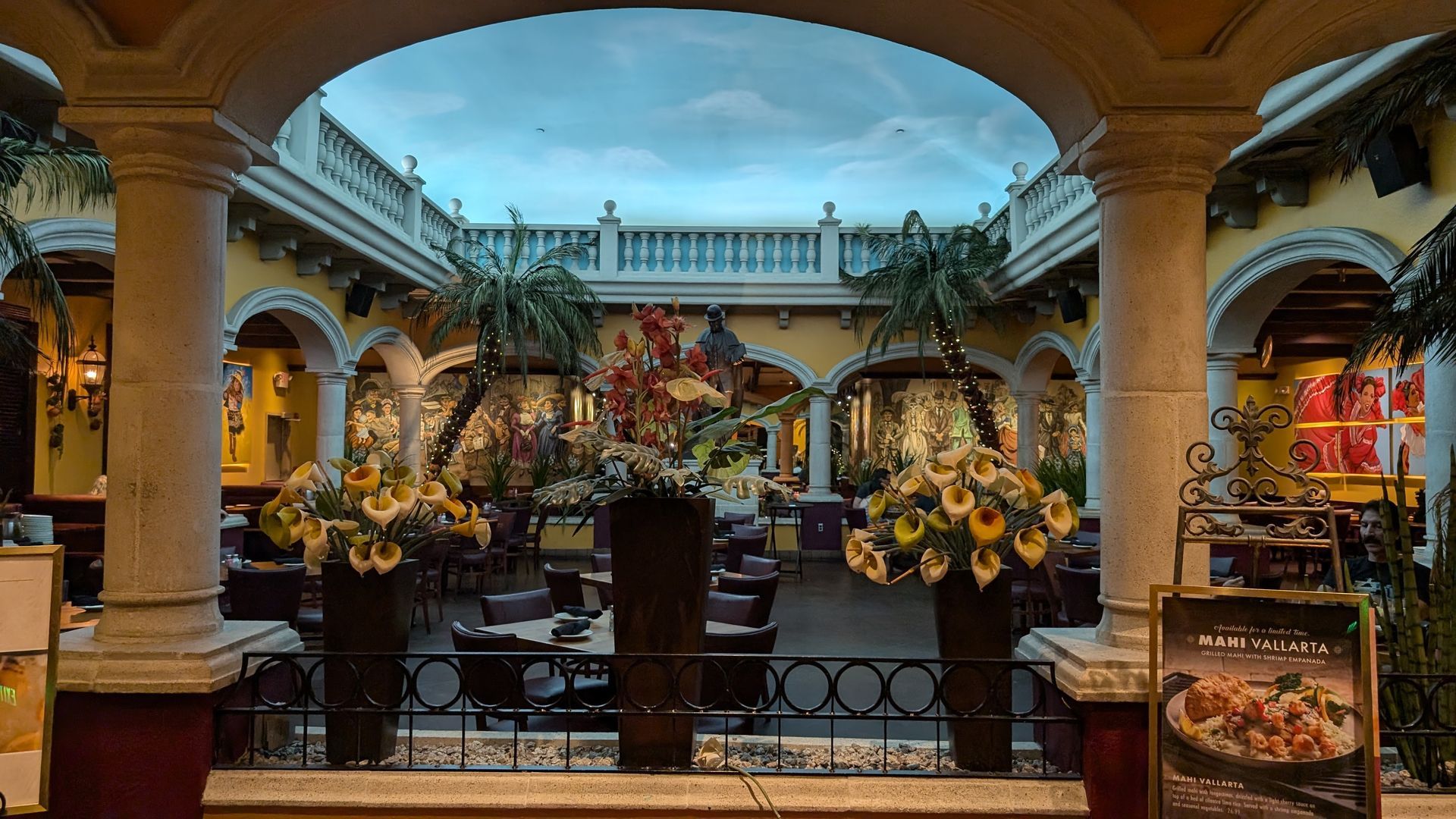 Restaurant interior with pillars, archways, floral displays, and a painted sky ceiling.