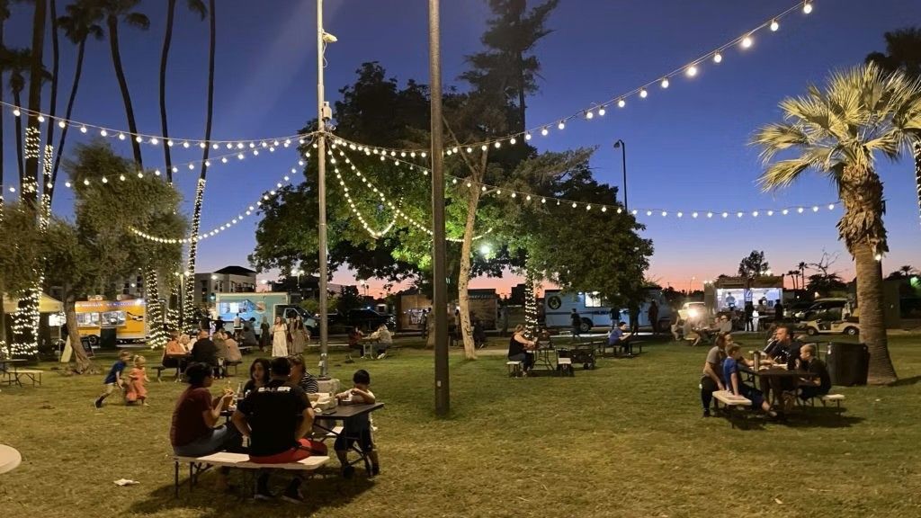 Nighttime food truck park with string lights; people eating at picnic tables.