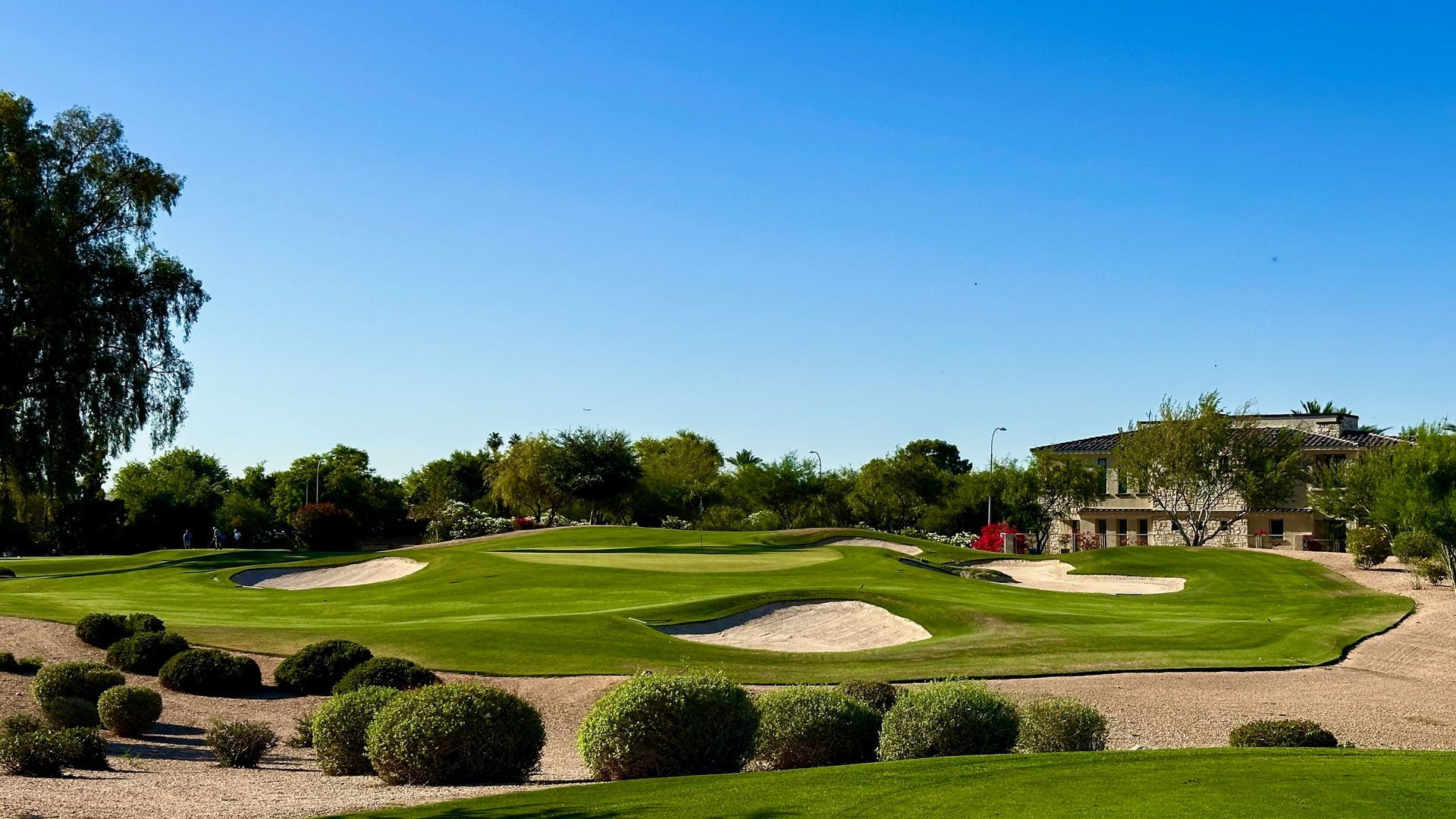 Golf course with green grass, sand traps, and clear blue sky.