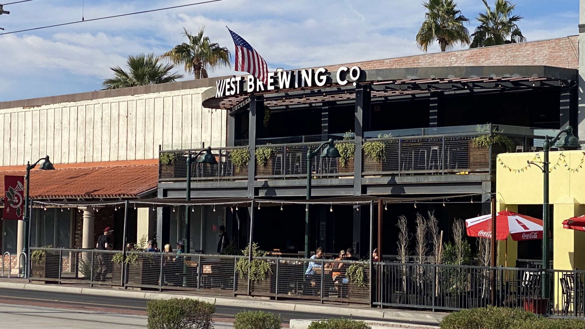 Exterior of 1st Brewing Co. with outdoor seating, an American flag, and palm trees.