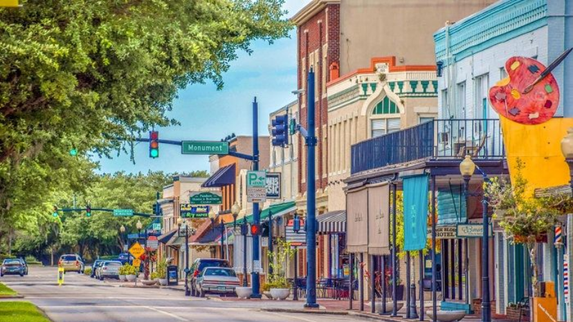Street scene with shops, trees, traffic lights, and a colorful building in a town.