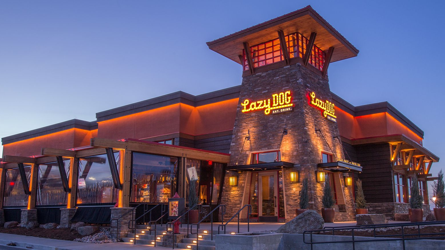 Restaurant exterior at dusk with warm lighting on stone and wood.