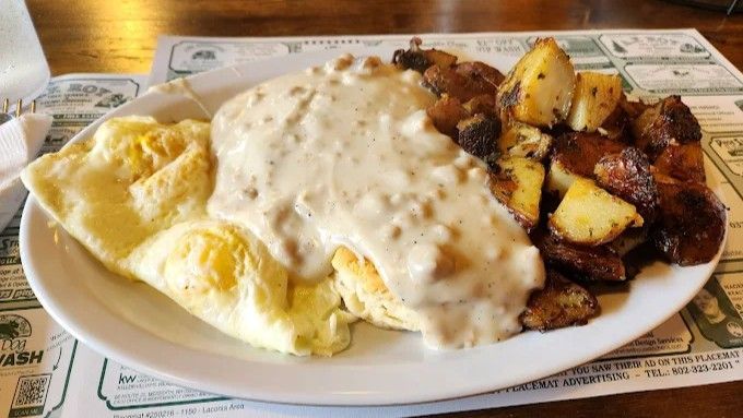 Plate of breakfast: scrambled eggs, biscuits with gravy, and fried potatoes.