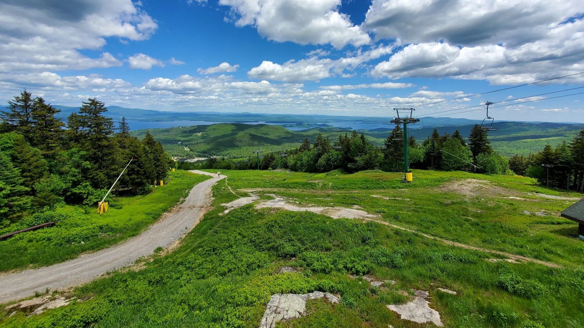 Green hillside ski slope under a blue sky, with lift towers and distant mountains.