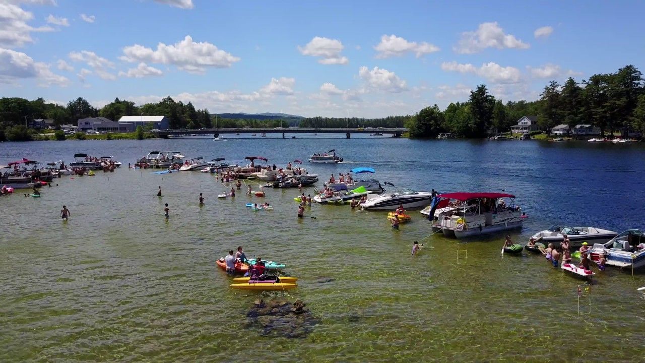 Boats and people enjoying a sunny day on a lake, near a bridge and shoreline.
