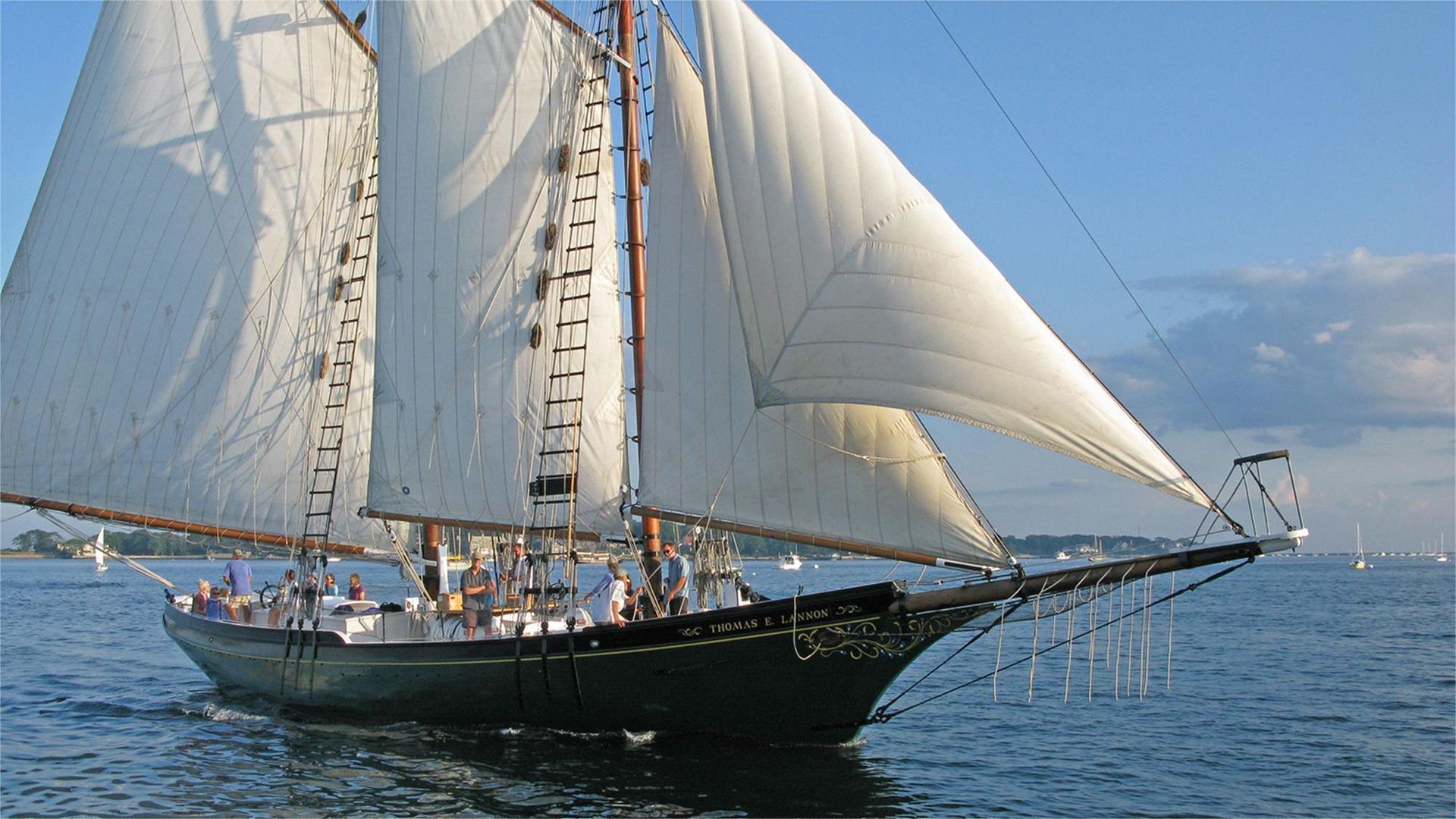 Schooner sailing on blue water with white sails billowing.