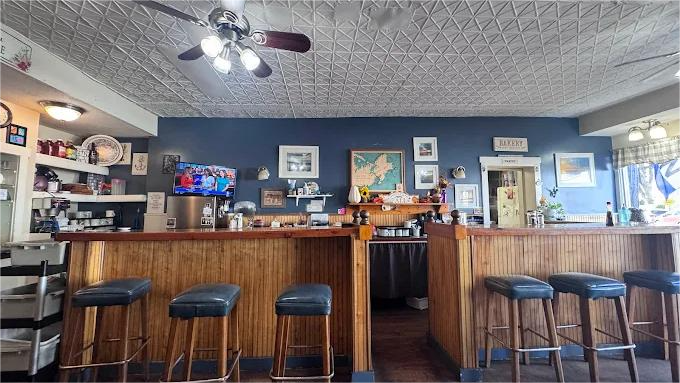 Interior of a diner with a wooden bar, stools, and decorations on blue walls. A ceiling fan hangs above.
