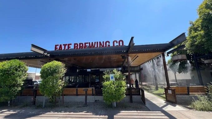 Exterior view of Fate Brewing Co. building with a red sign against a blue sky, trees in the foreground.