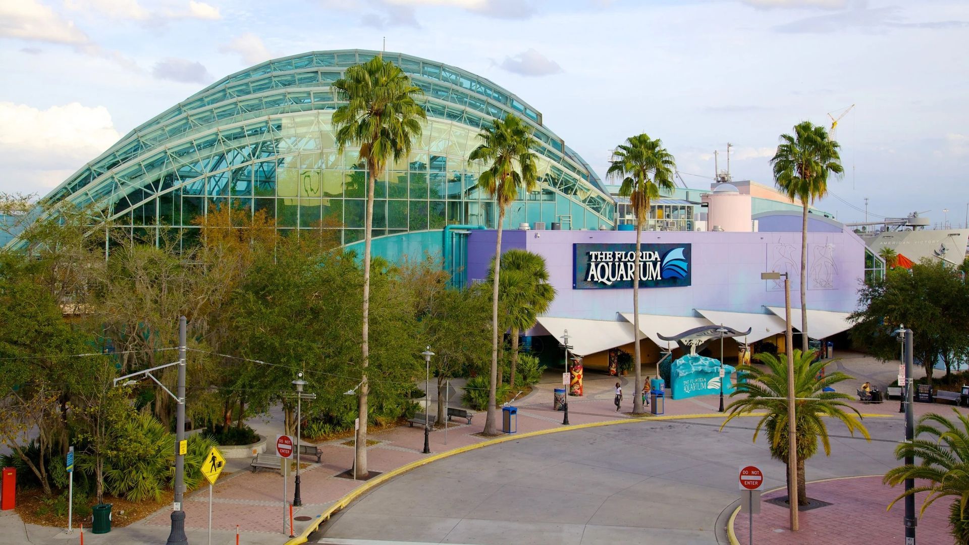 Exterior view of an aquarium building with a large glass dome and palm trees. Blue and purple colors.