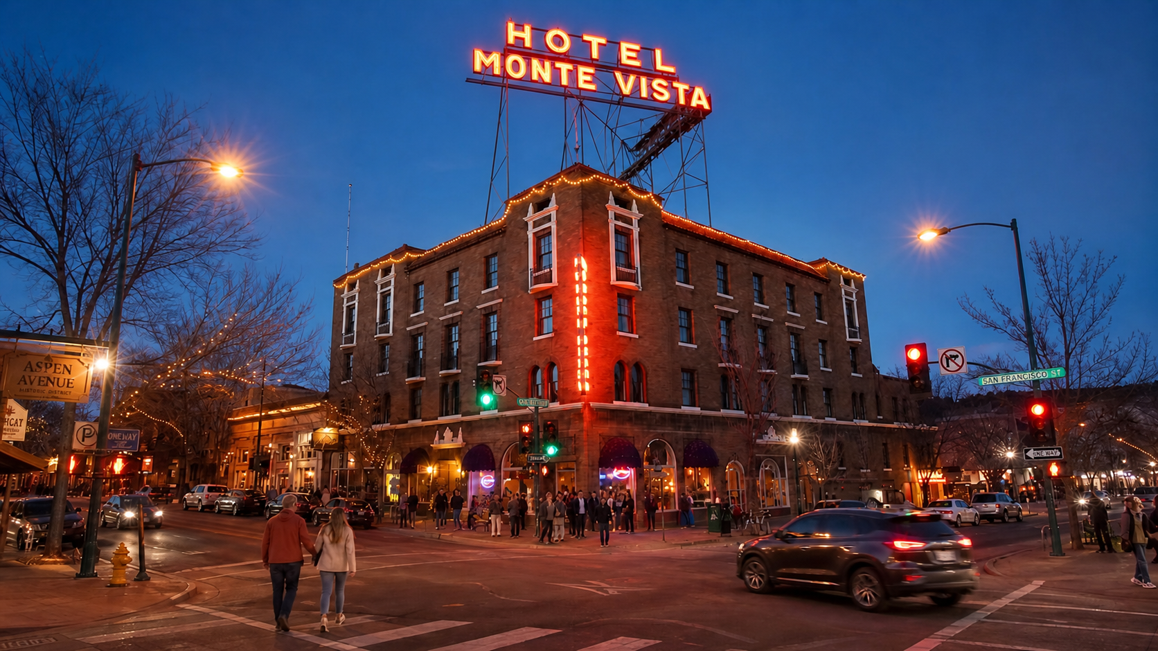 Hotel Monte Vista lit up at dusk on a city street with cars and pedestrians nearby