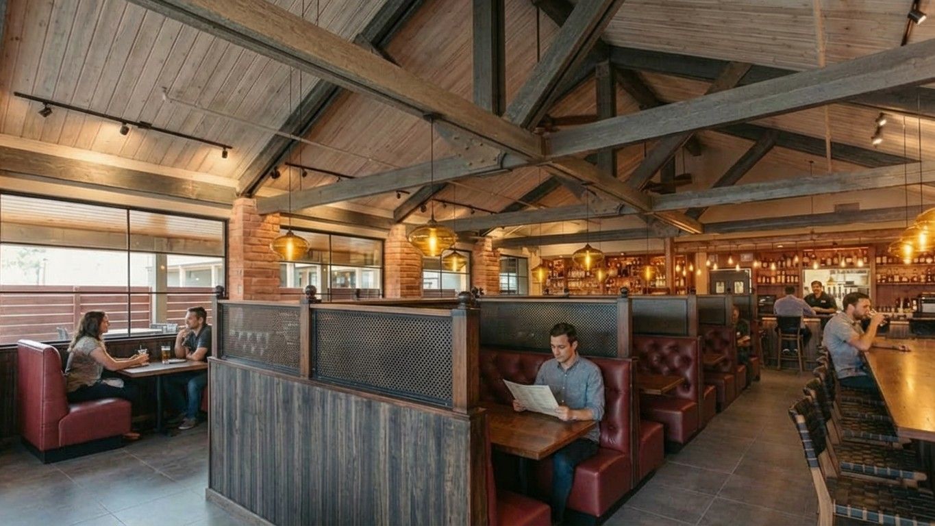 Rustic restaurant interior with wooden vaulted ceilings, pendant lights, booths with leather seating, and patrons.