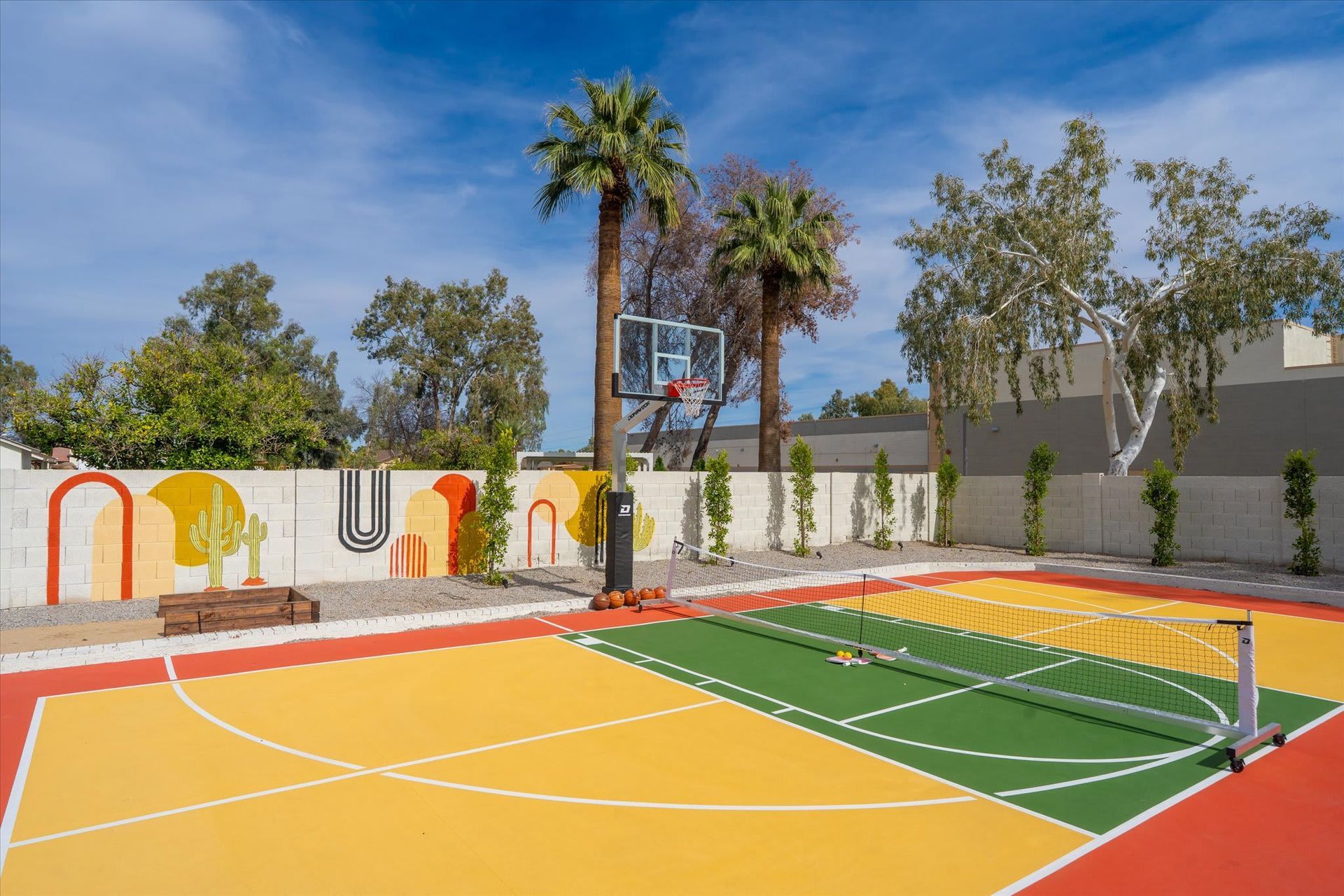 Colorful outdoor pickleball court with a net, palm trees, and a bright mural along the wall