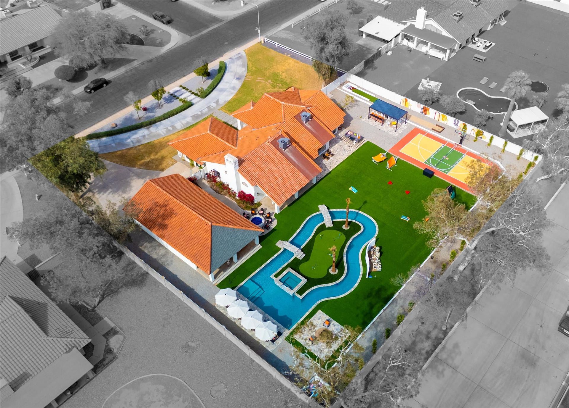 Aerial view of a school campus with orange-roofed buildings, a green field, playground, and swimming pool.