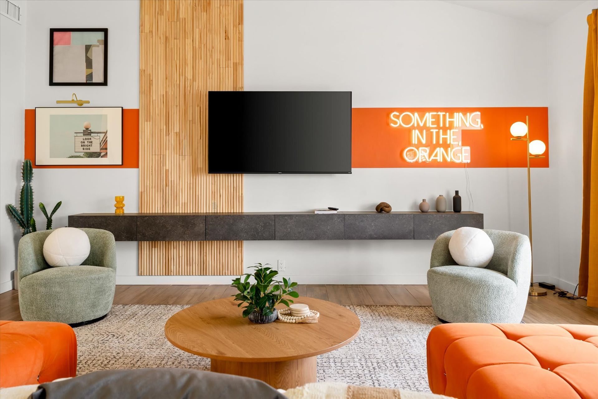 Modern living room with TV, orange wall art, gray chairs, and a round wooden coffee table