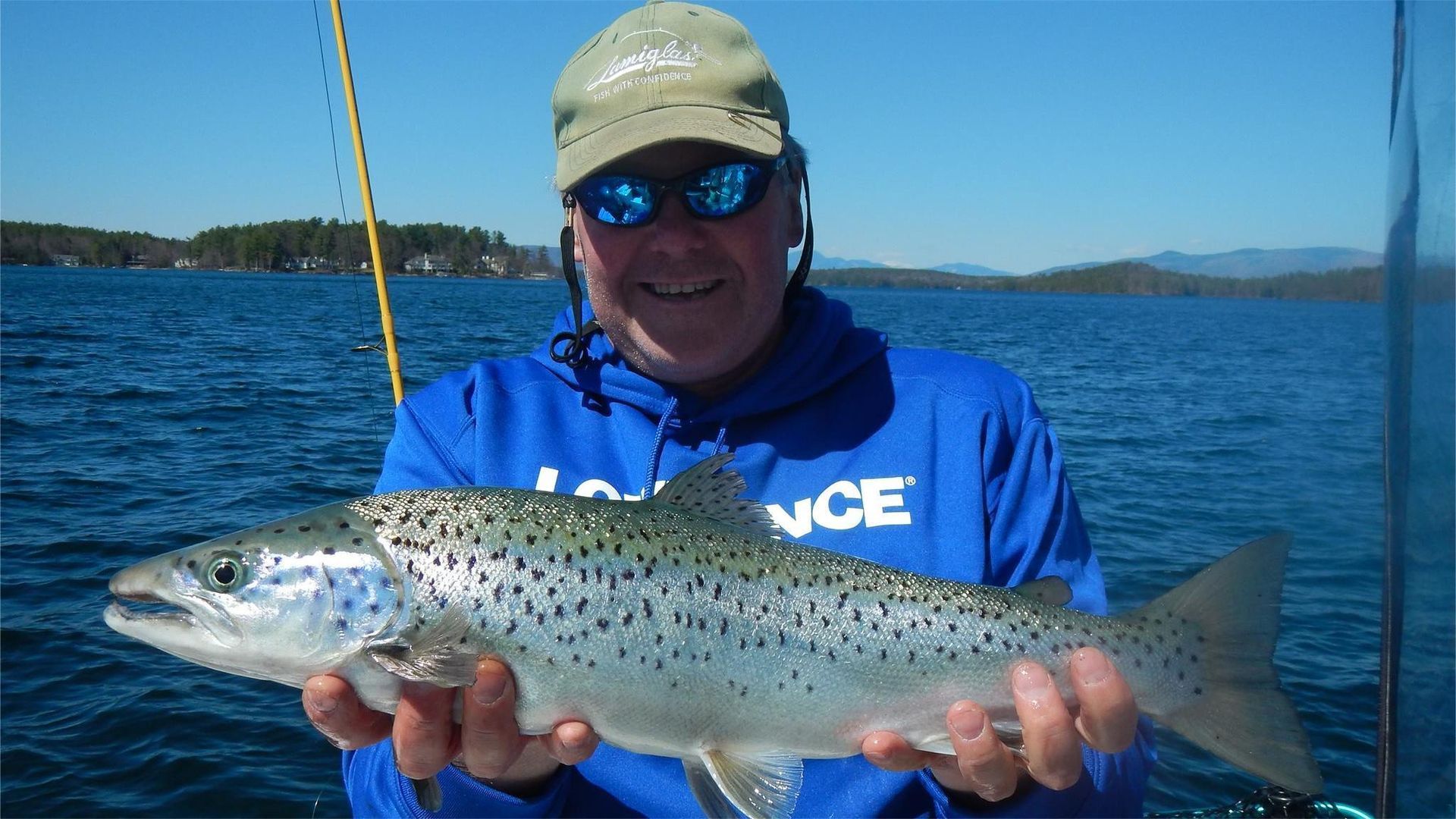 Man smiling, holding a speckled fish on a boat. Blue water and sky.