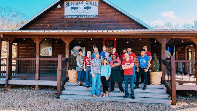 Group of people in front of the Buffalo Grill restaurant, smiling. Wooden exterior with a porch.