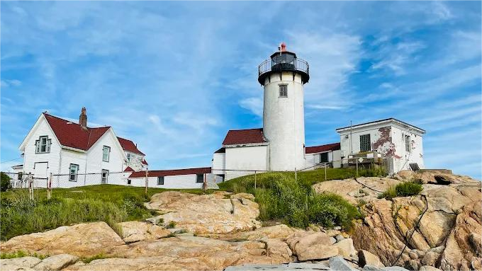 White lighthouse and buildings on rocky coastline under a blue sky.