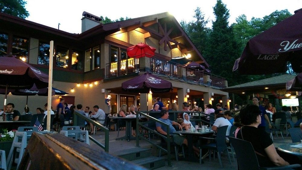 Outdoor restaurant patio with patrons seated at tables; building with balcony and string lights.