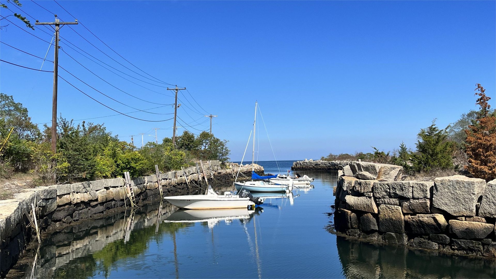 Boats docked in a narrow inlet between stone walls under a clear, blue sky.