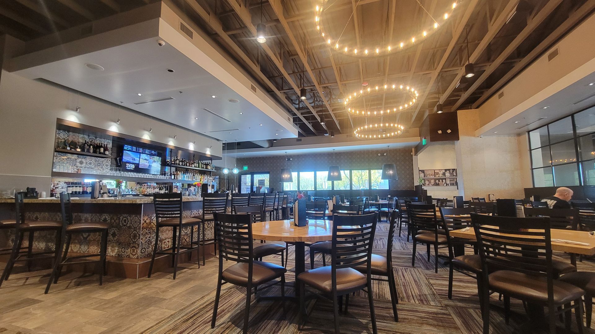Interior of a restaurant with a bar, tables, chairs, and decorative lights.