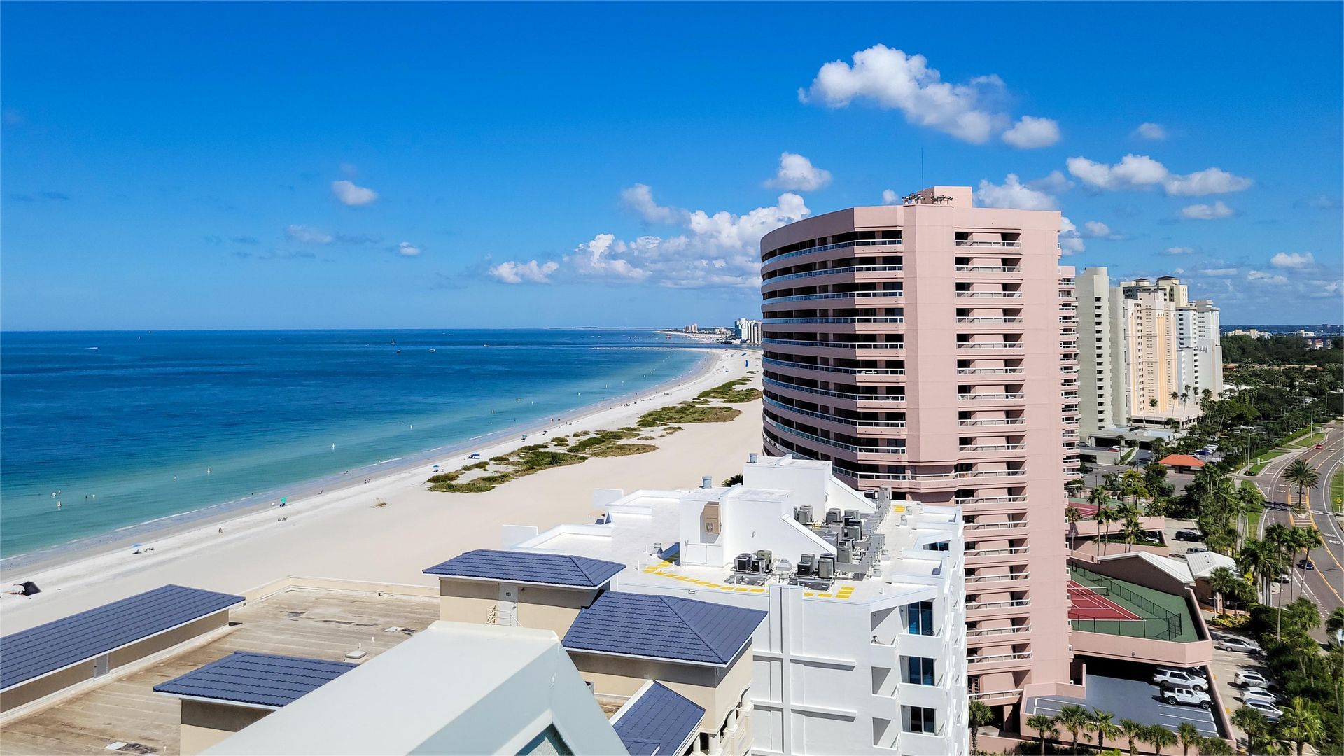 Beachfront high-rise buildings and sandy beach under a blue sky, with the ocean visible.