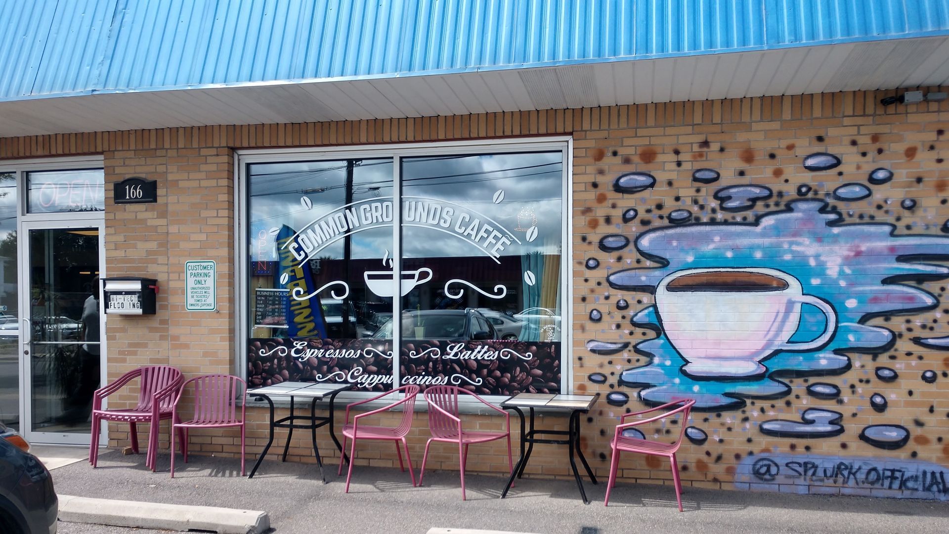 A coffee shop storefront with outdoor tables and a wall mural of a giant coffee cup against a starry, blue backdrop.