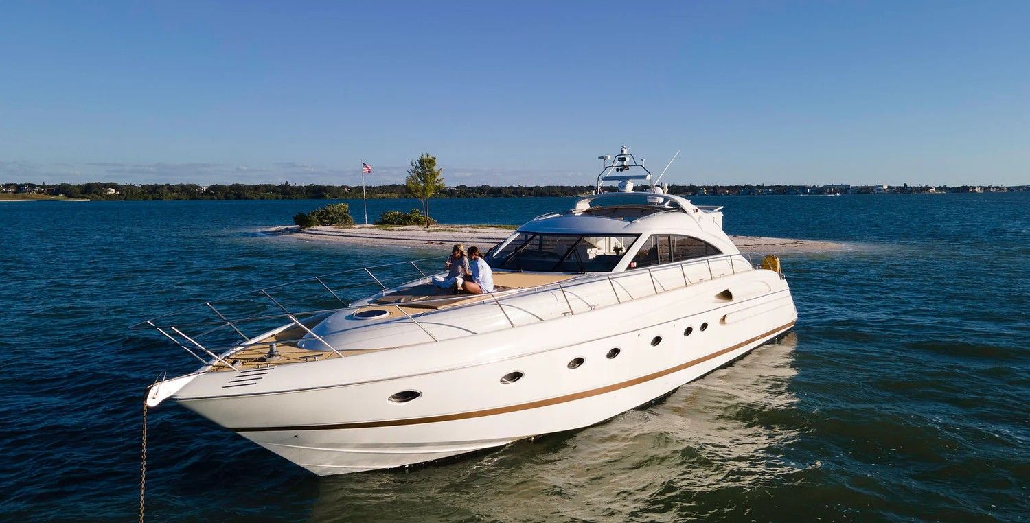 White motor yacht on blue water with two people on deck, island in background.