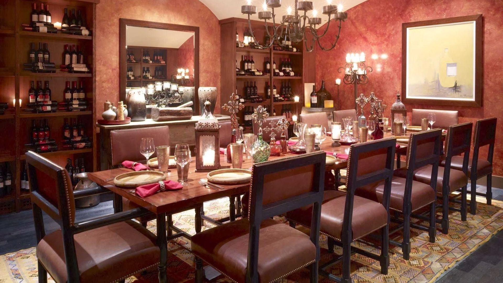 Elegant dining room set for a meal. Red walls, wine racks, long table with place settings, and chairs.