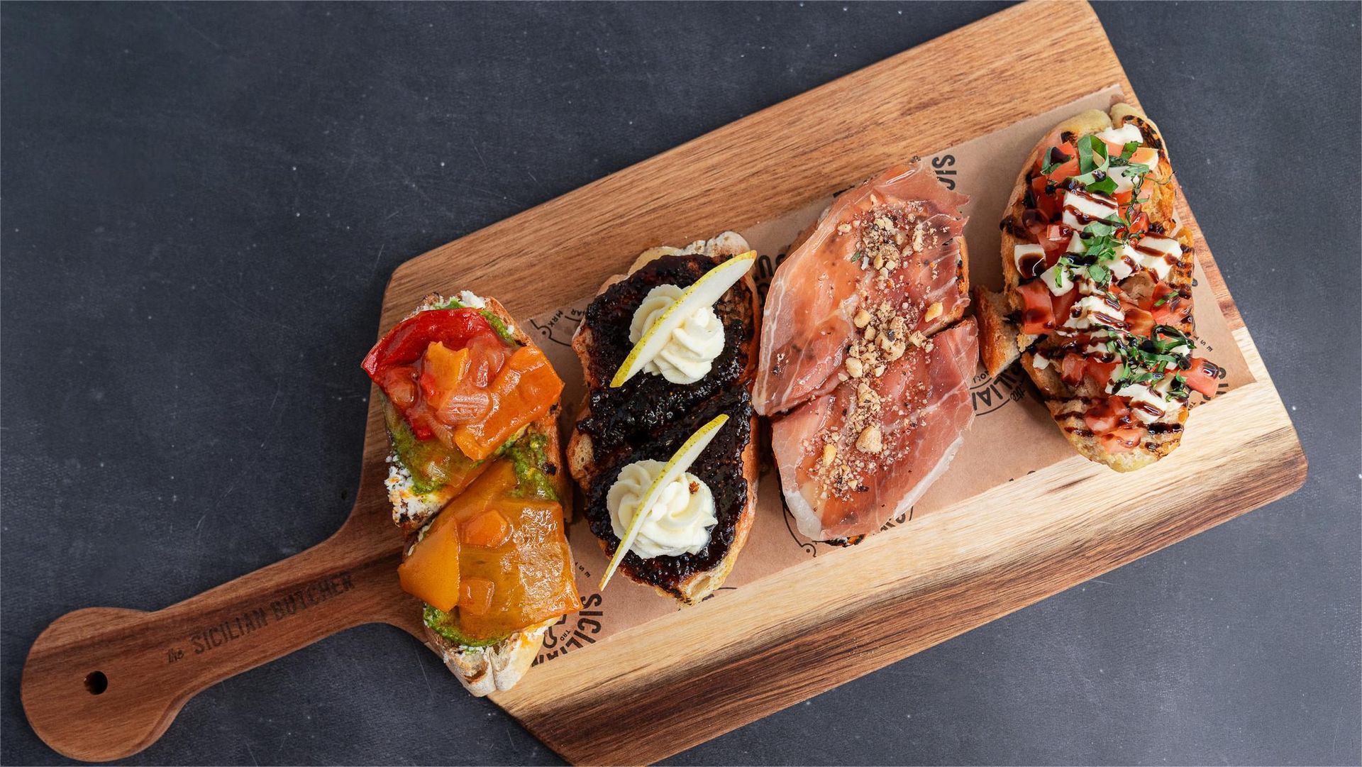 Assortment of toasted bread slices topped with various ingredients on a wooden board.