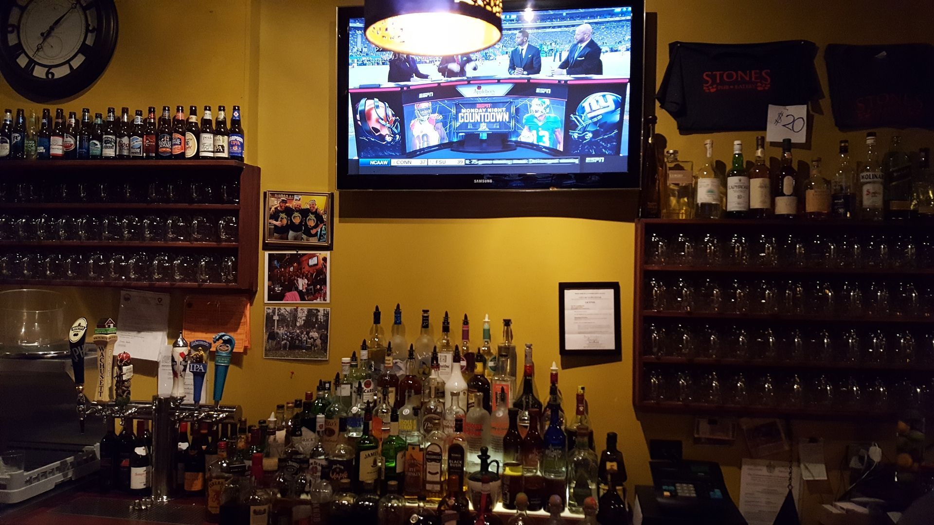 Bar interior with liquor bottles, glasses, and a TV showing a sports program.