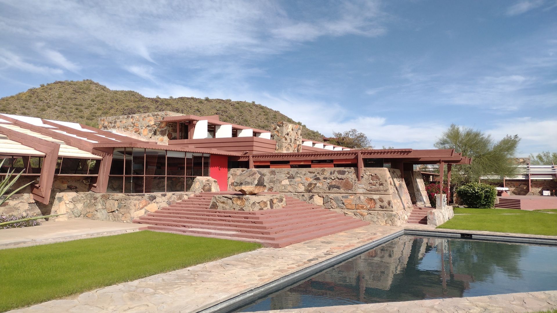 Frank Lloyd Wright’s Taliesin West in Arizona, with stone walls, red accents, a pool, and a mountain backdrop.