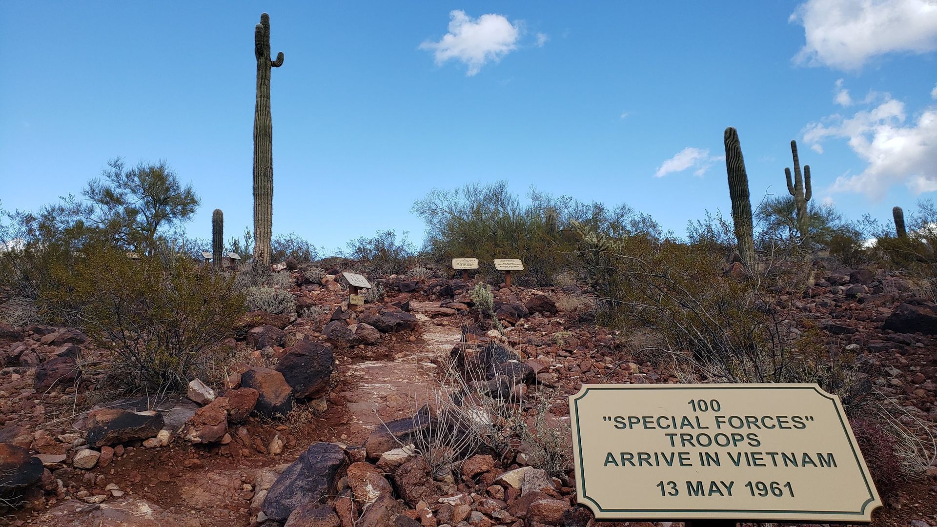 Sign marking the arrival of 150 Special Forces troops in Vietnam on a rocky desert path with cacti.